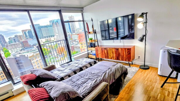 A modern bedroom with a large bed, a TV, a desk, and a view of a cityscape. - Downtown Escape – Walk to Cruise Ships & BC Place | 3 Comfy Beds (Vancouver)