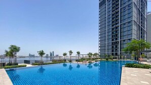 A swimming pool with clear blue water, surrounded by a modern building and a view of a city skyline. - Creek Edge - One Bedroom with Partial Sea View (Creek Harbour)