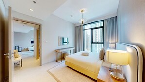 A modern hotel room with a large bed, a desk, a chair, and a view of the city through large windows. - Creek Edge - One Bedroom with Partial Sea View (Creek Harbour)