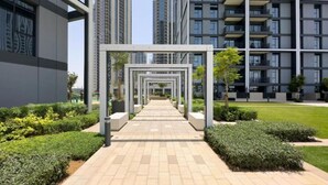 A pathway leading to a modern building with a series of balconies and a well-maintained garden area. - Creek Edge - One Bedroom with Partial Sea View (Creek Harbour)