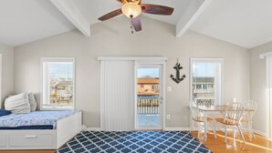 Una habitación con cama, una mesa de comedor con sillas, un ventilador de techo y vistas por una puerta.