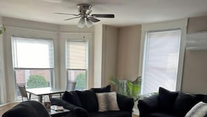 Ein Wohnzimmer mit einer schwarzen Sofagarnitur, einem runden Couchtisch und einem Deckenventilator.