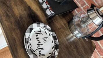 Un taulell de cuina amb una cafetera, una tassa, un plat amb la frase 'be thankful' escrita i una safata amb tasses de cafè.