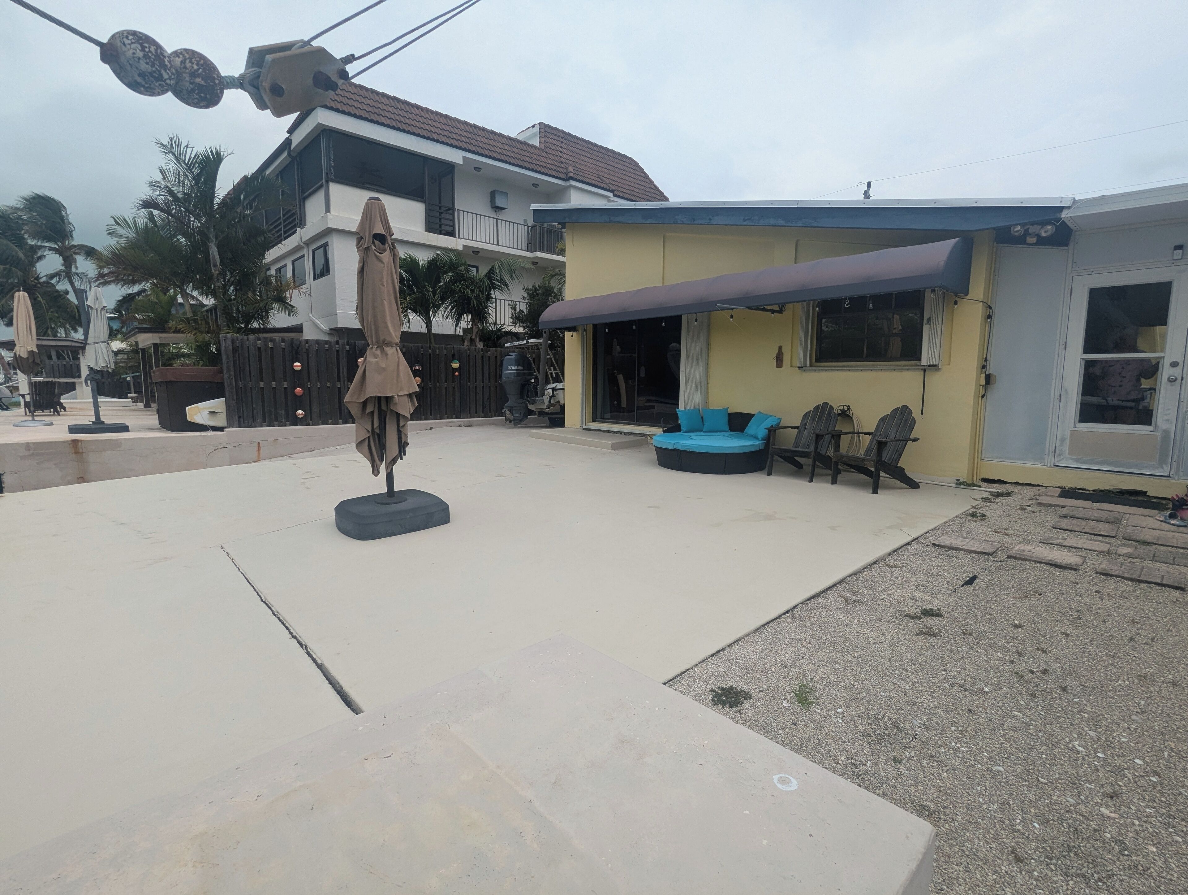 A residential area with a paved patio, a beige umbrella, a blue sofa, and two wooden chairs.