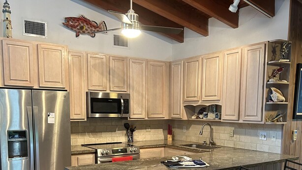A modern kitchen with wooden cabinets, stainless steel appliances, a central island with bar stools, and pendant lighting. - Deep Water Home located in White Marlin Beach Neighborhood (Islamorada)
