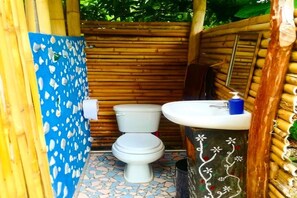 Et lille, lukket badeværelse med toilet og vask, vægge af bambus og flisegulv.
