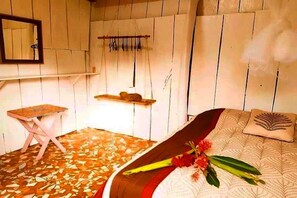 A room with a bed, a small table, a mirror, and a shelf with items.