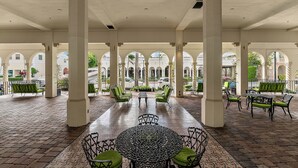 A covered outdoor seating area with a patterned table and chairs, surrounded by columns and arches.