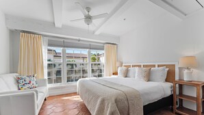 A hotel room with a bed, a white sofa, a wooden nightstand, and a window with curtains.