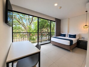 A hotel room with a bed, a desk, and a large window with a view of trees and a street. - Hotel ECO 44 (Medellín)