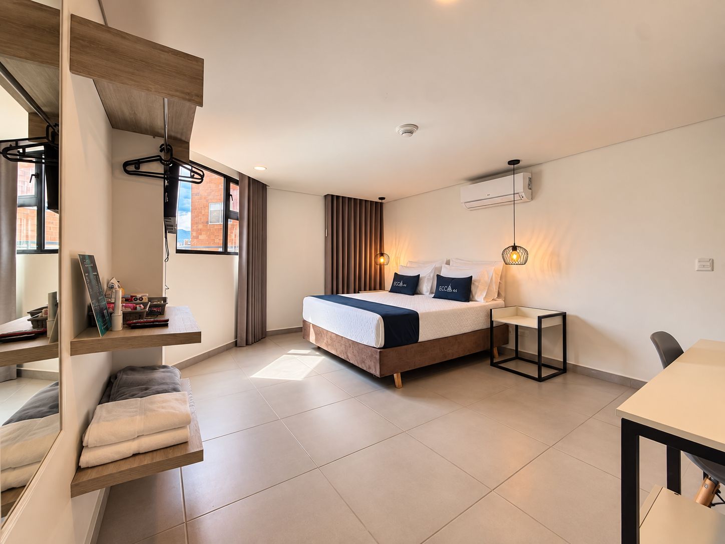 A modern hotel room with a bed, bedside table, and a desk with a chair.