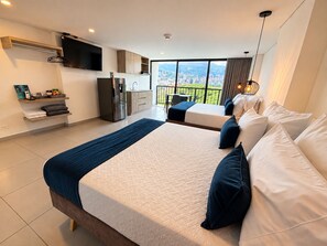 Habitación de hotel moderna con una cama grande, kitchenette, televisión de pantalla plana y balcón con vista a la ciudad.