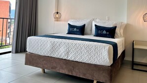 A modern bedroom with a large bed, a hanging light fixture, and a view of the city through a large window. - Hotel ECO 44 (Medellín)