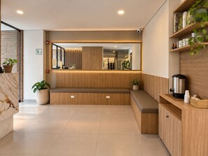 A modern reception area with a marble counter, wooden seating, a large mirror, and a coffee machine. - Hotel ECO 44 (Medellín)