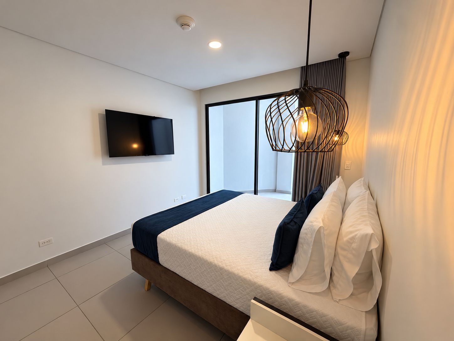 A modern bedroom with a large bed, a mounted TV, and a unique hanging light fixture.