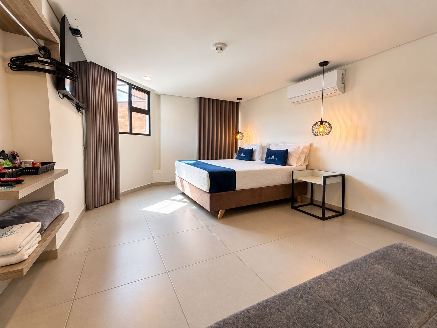 Un dormitorio moderno con cama, mesitas de noche, un escritorio y una lámpara colgante.