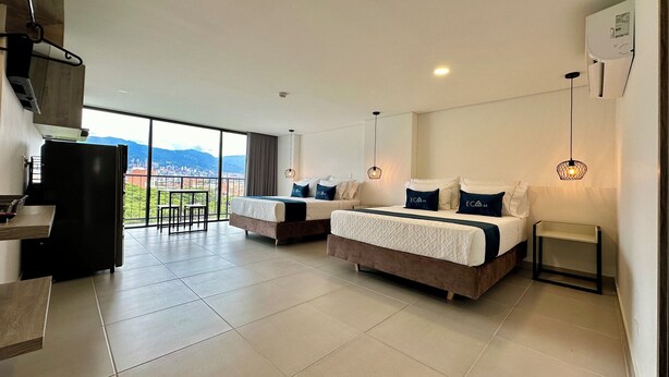 A modern hotel room with two beds, a dining area, and a view of the city. - Hotel ECO 44 (Medellín)