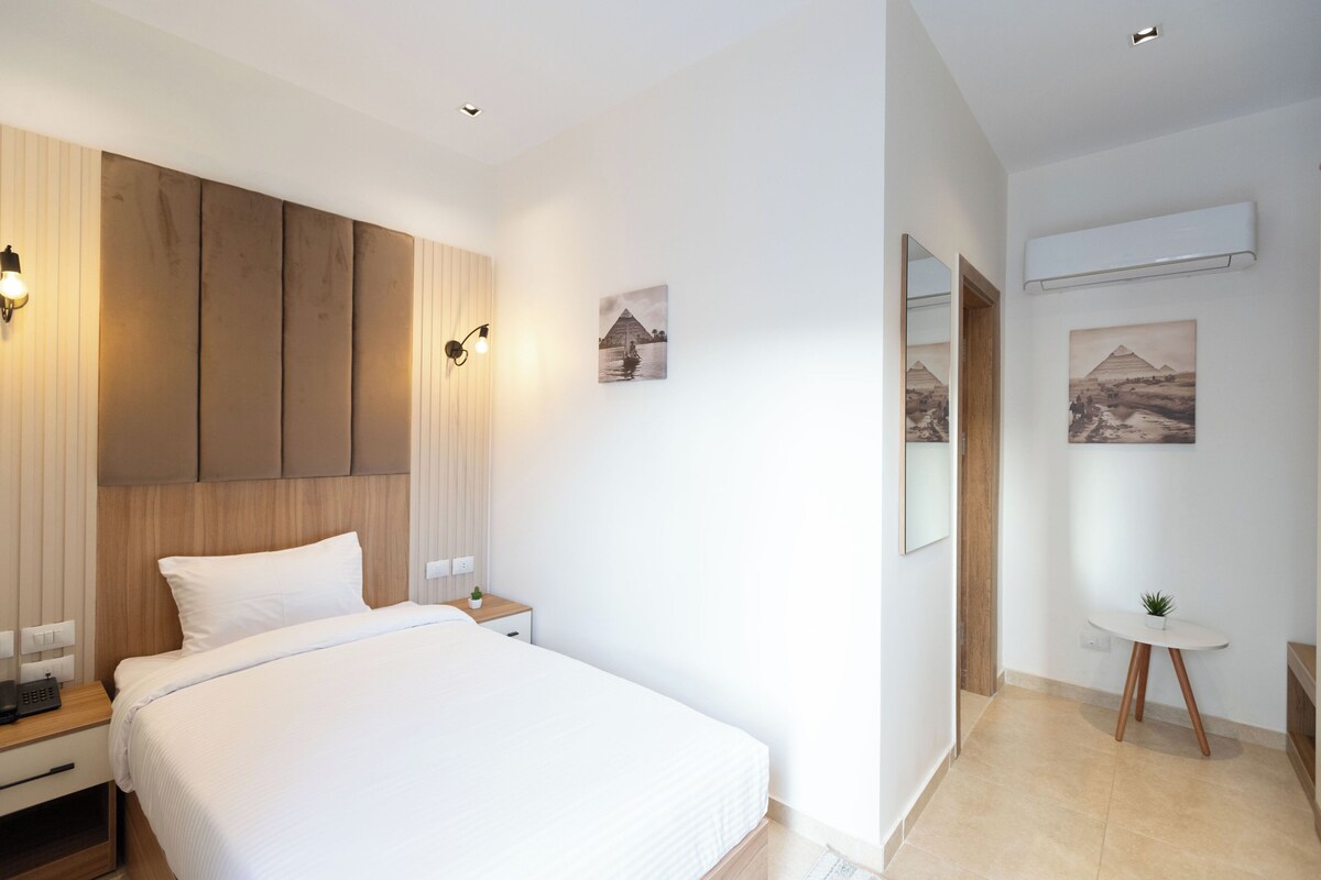 Une chambre d’hôtel moderne avec un grand lit, une tête de lit en bois, des tables de chevet et des œuvres d’art accrochées au mur.