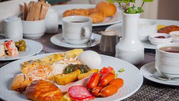 A breakfast setting with plates of food, cups, and a vase with a plant.
