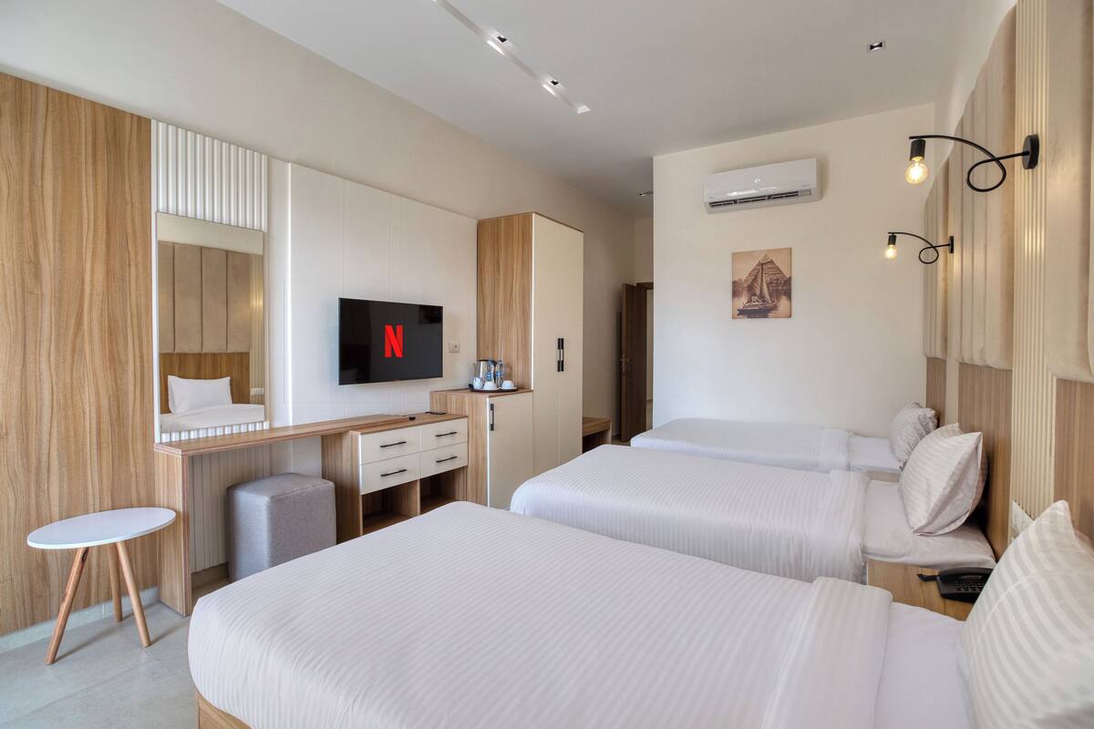 A hotel room with two beds, a desk with a TV, a small table, and a wardrobe.
