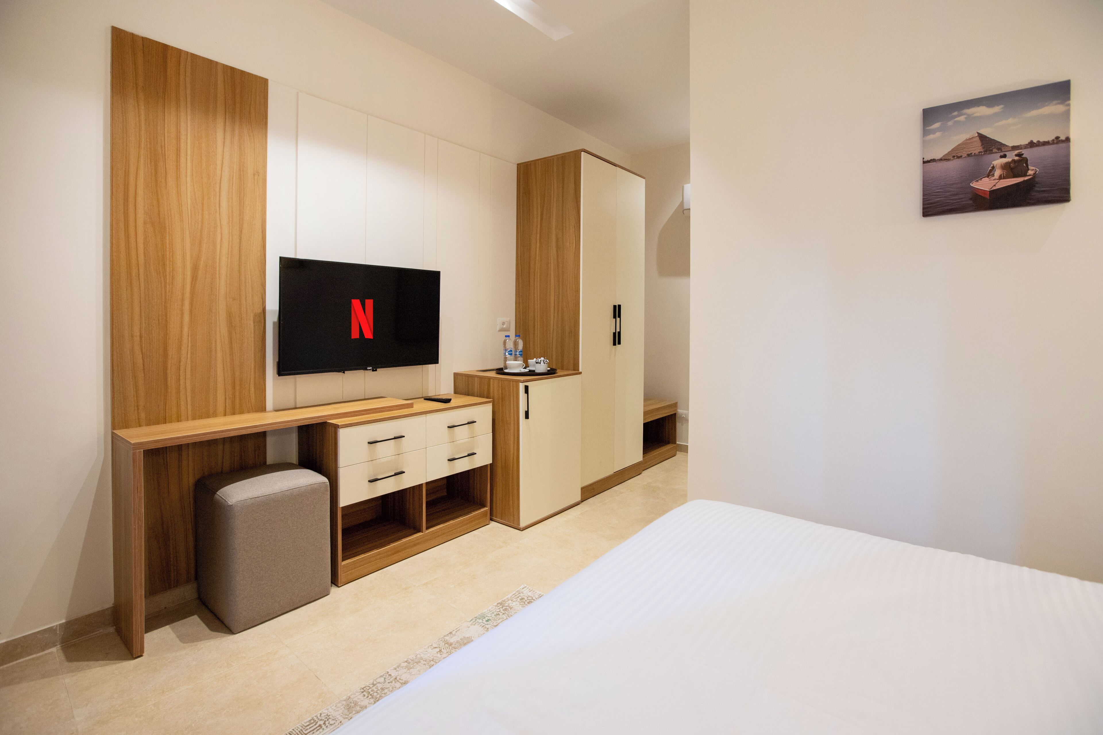 A modern hotel room with a wooden desk, a flat-screen TV, a wardrobe, and a bed.