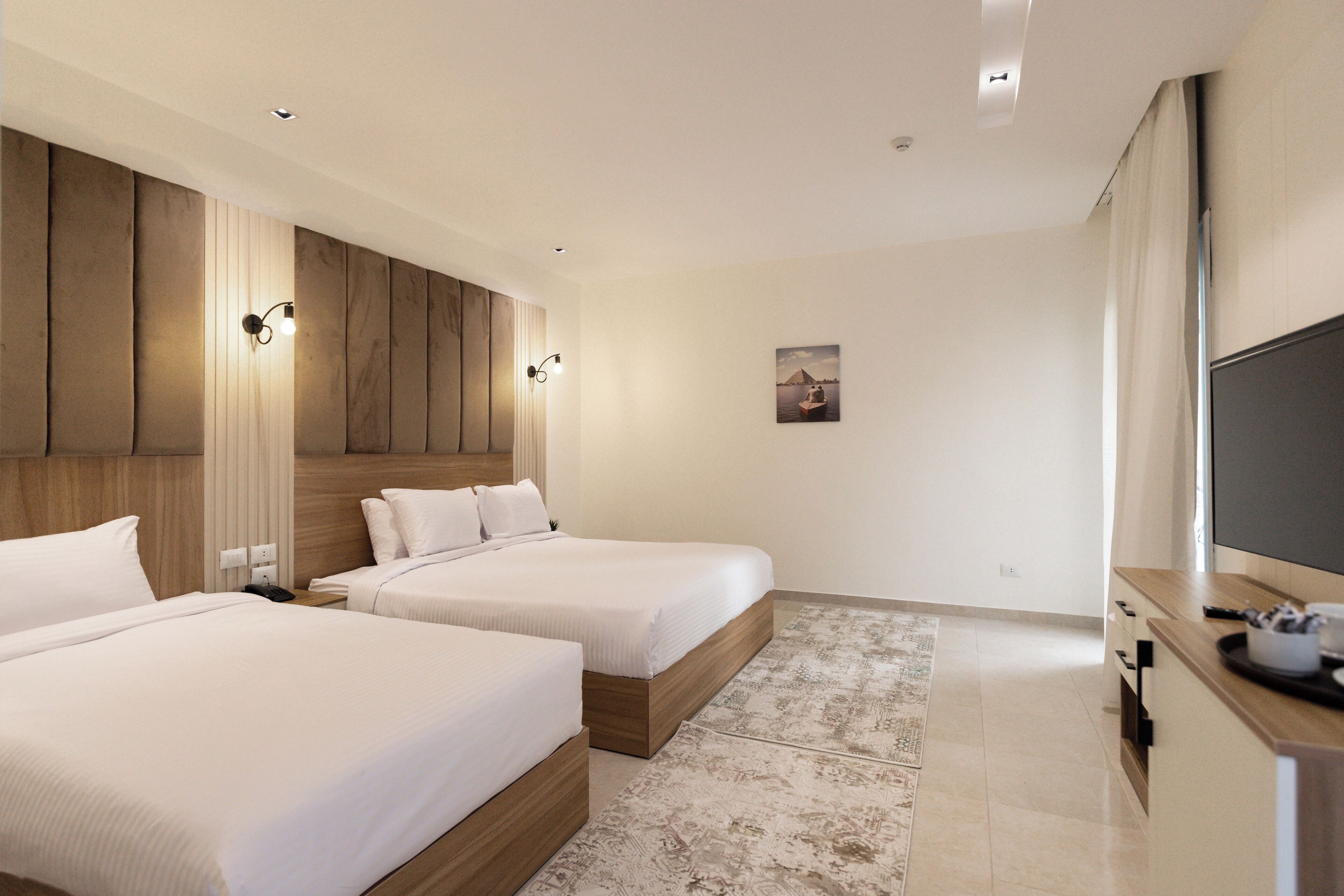 A hotel room with two beds, a wooden headboard, a flat-screen TV, and a small desk with a cup and remote control.