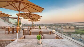 A rooftop terrace with outdoor seating, umbrellas, and a view of the cityscape.