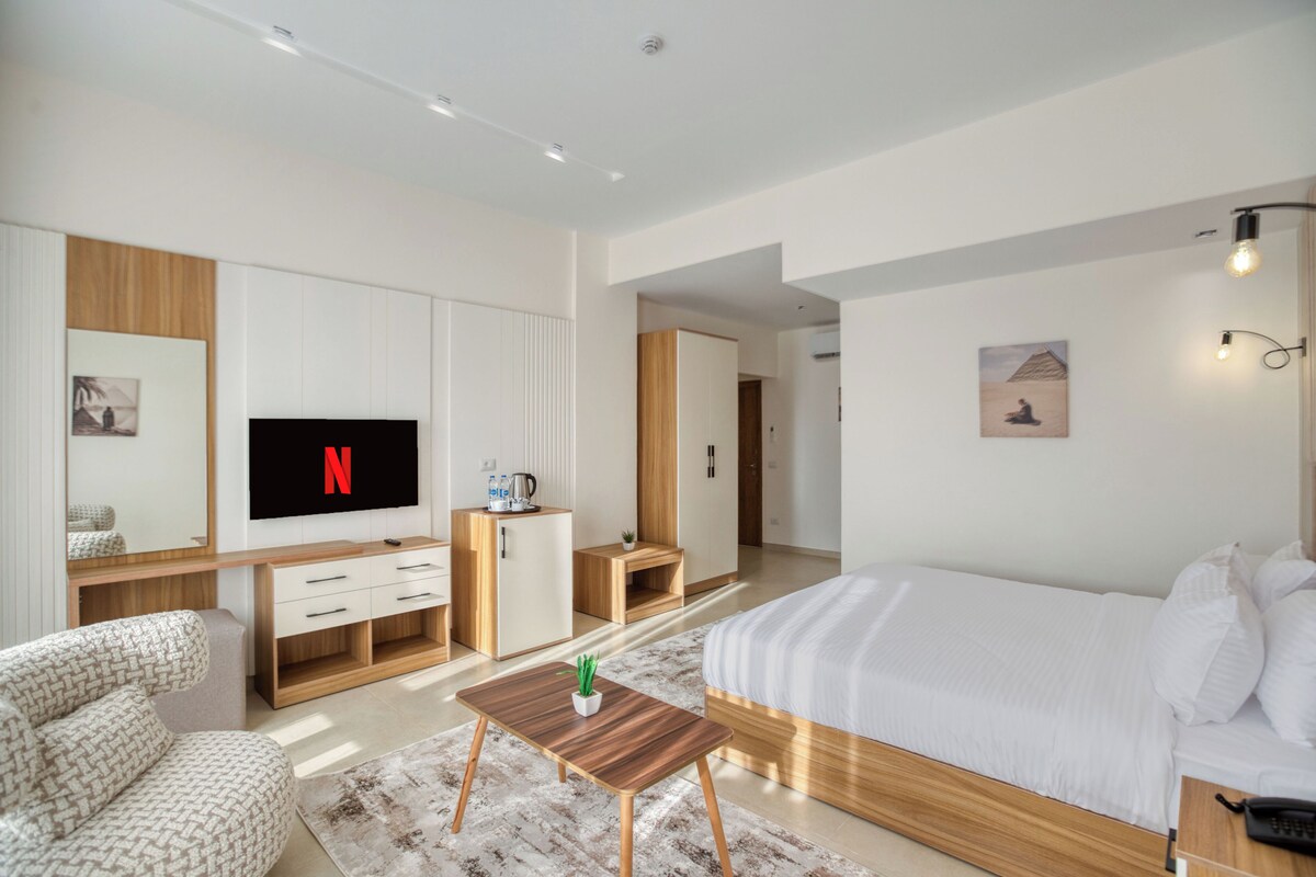 Une chambre d’hôtel moderne dotée d’un grand lit, d’une télévision, d’un bureau en bois, d’un canapé et d’une petite table sur laquelle est posée une plante.