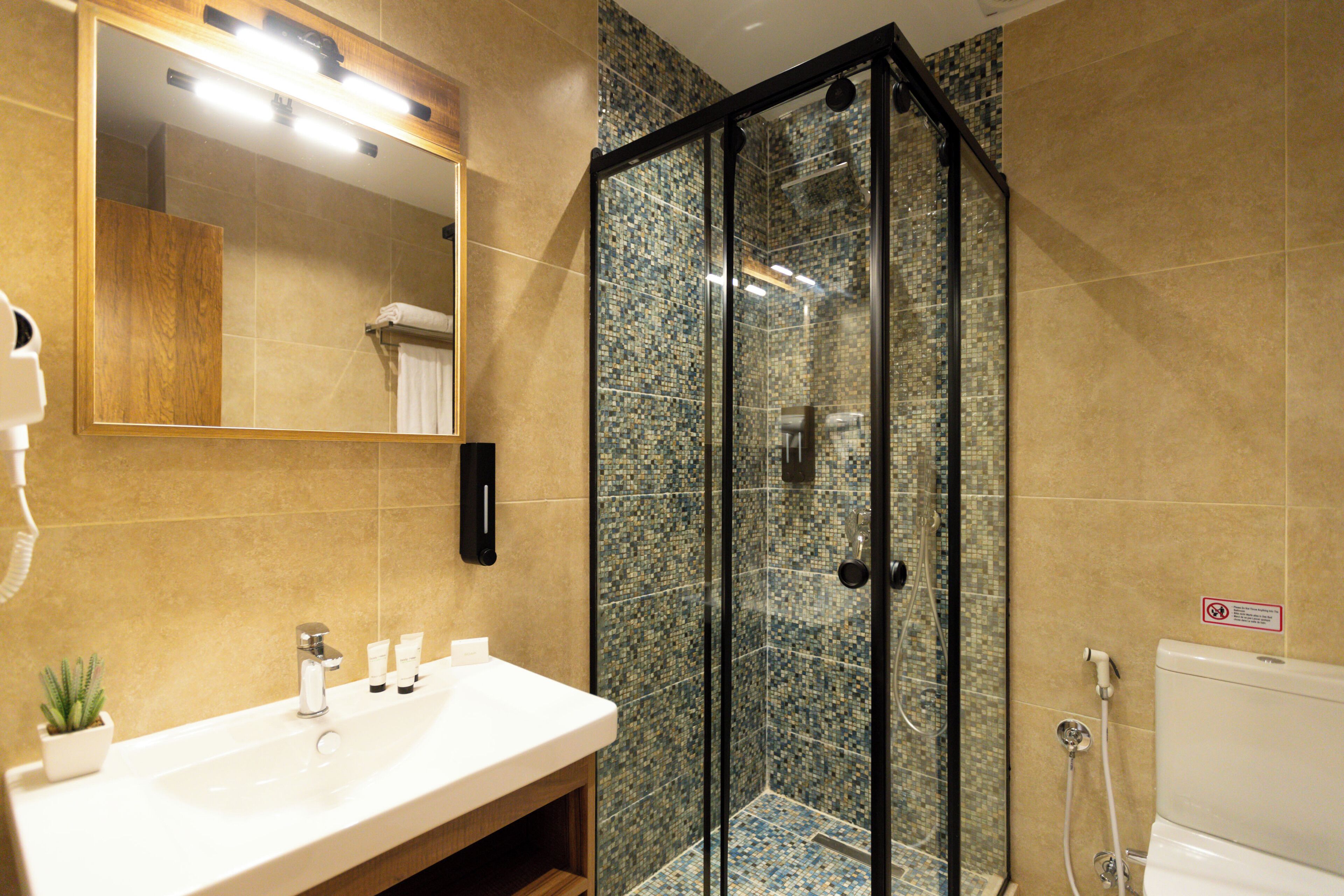 A bathroom with a glass-enclosed shower, a sink with toiletries, and a mirror.