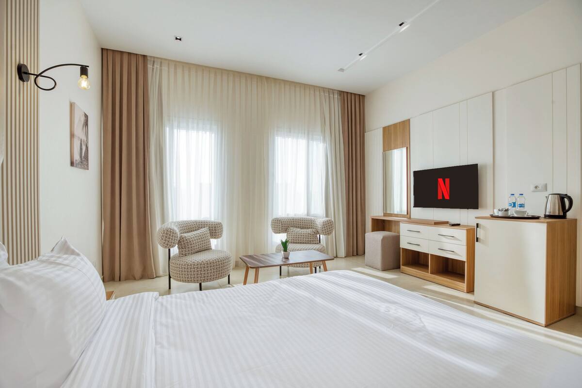 A hotel room with a bed, two armchairs, a coffee table, a TV, and a minibar.