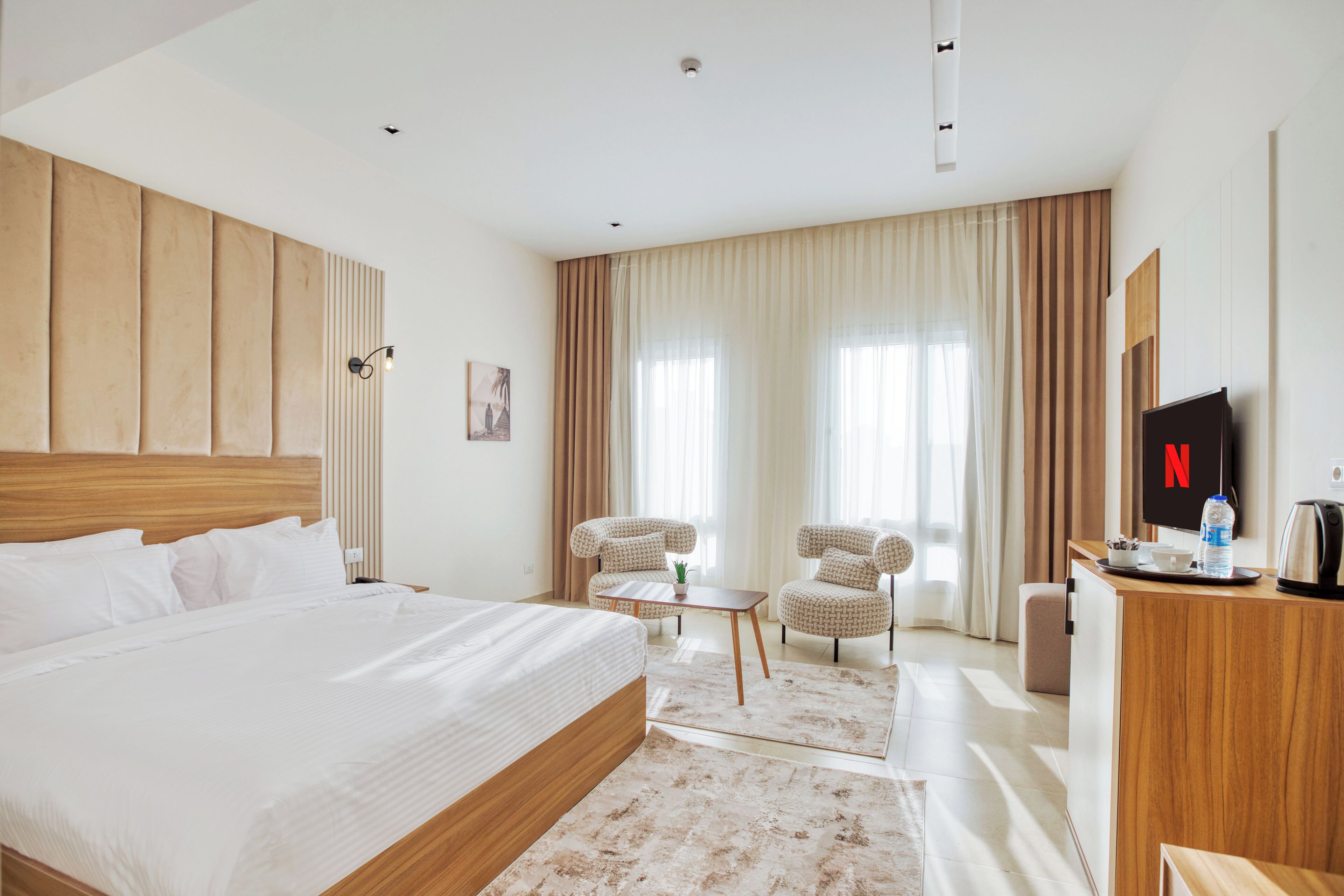 Habitación de hotel con una cama grande, dos sillones, una mesita, televisor y minibar.