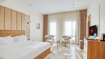 Habitación de hotel con una cama grande, dos sillones, una mesita, televisor y minibar.