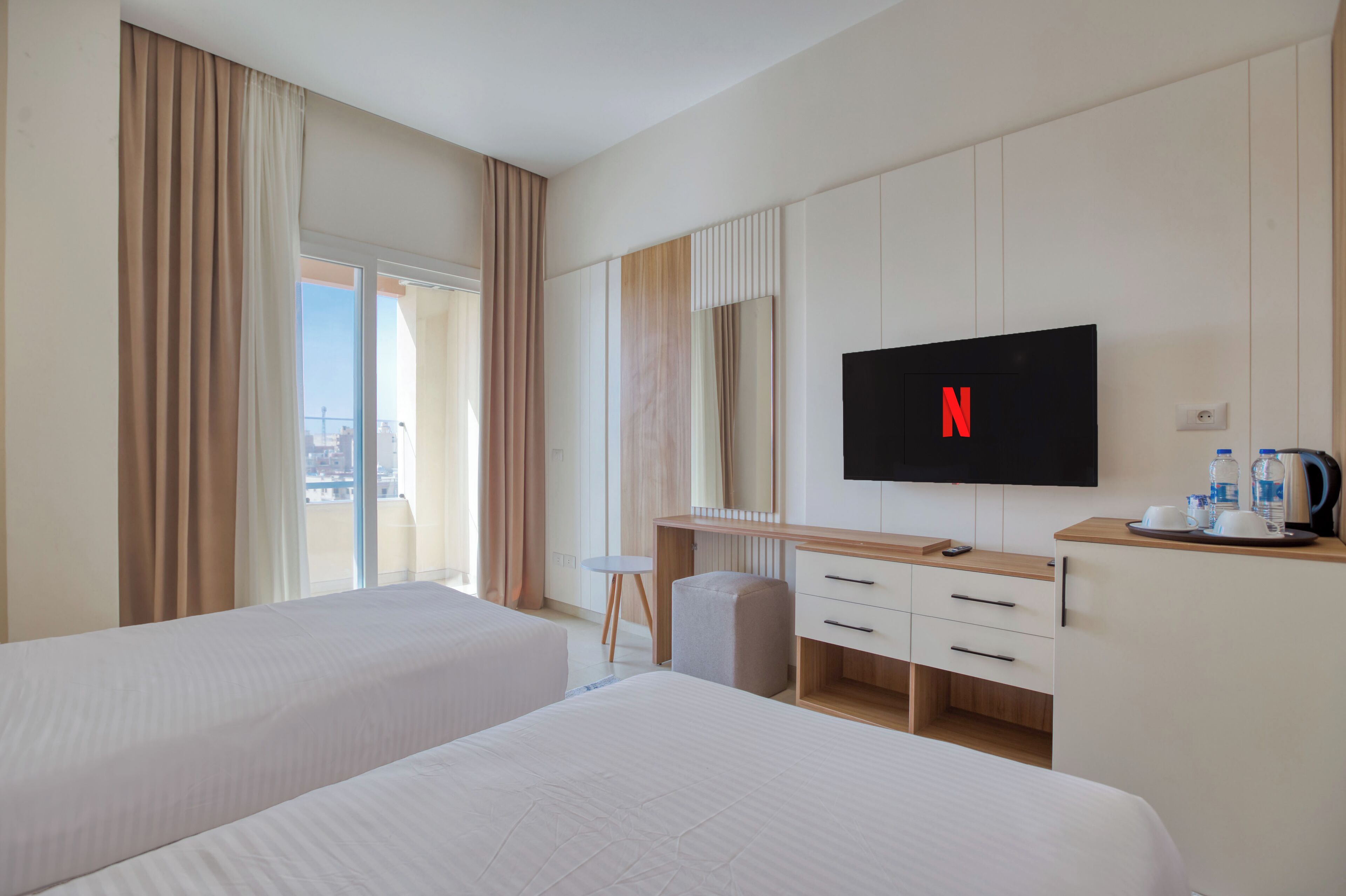 A hotel room with two beds, a desk, a TV, and a city view.
