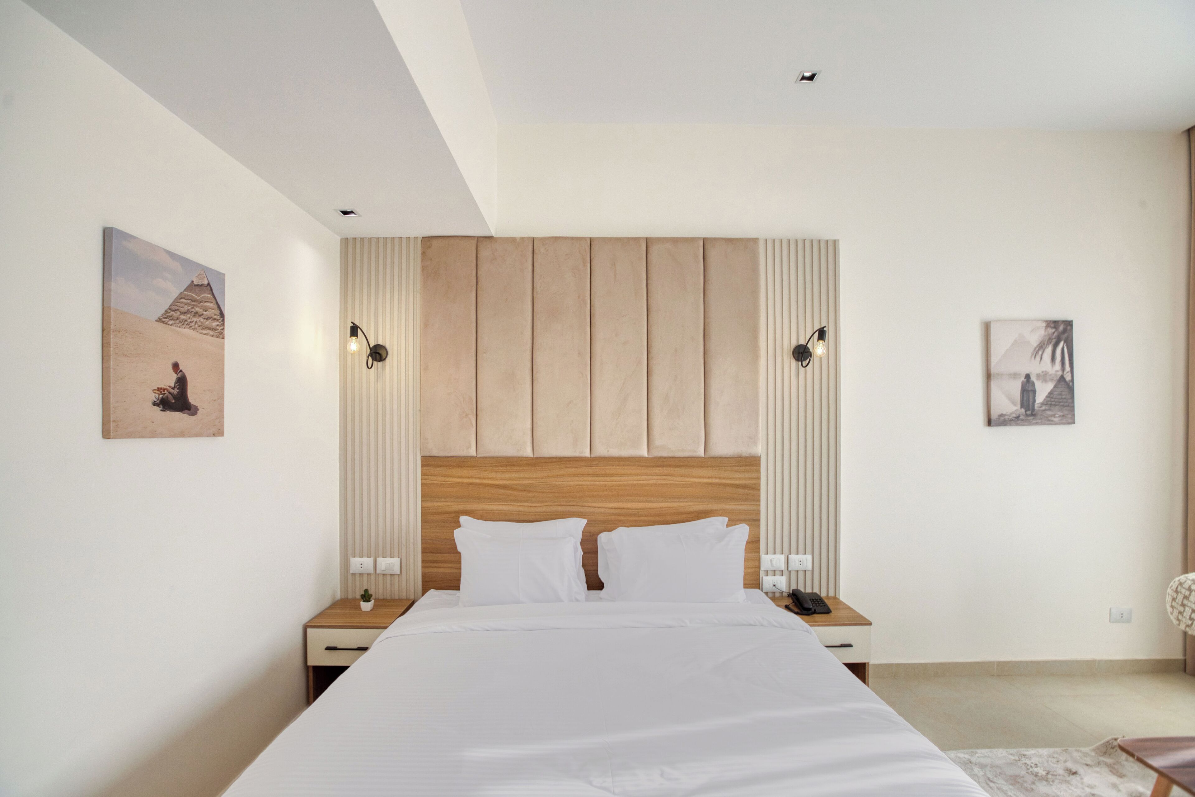 Une chambre d’hôtel moderne avec un grand lit, une tête de lit en bois et deux tables de chevet avec des lampes.