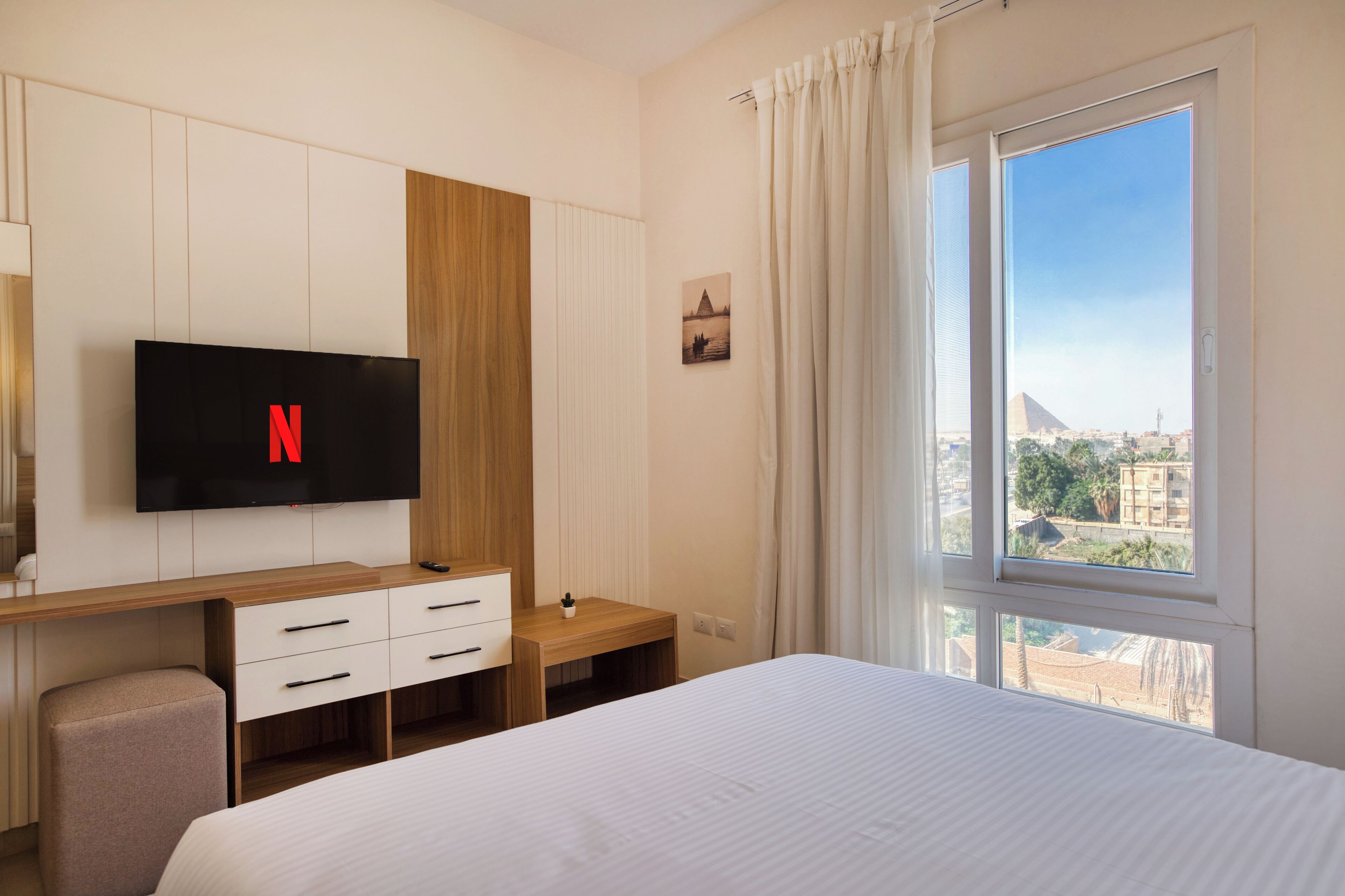 Hotelkamer met een bed, een bureau met een tv waarop het Netflix-logo staat, een raam met gordijnen en uitzicht op een stadsbeeld.
