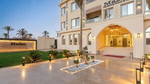 A hotel entrance with a well-lit facade, a palm tree, and a clear sky. - Mazar Pyramids Hotel (Giza)