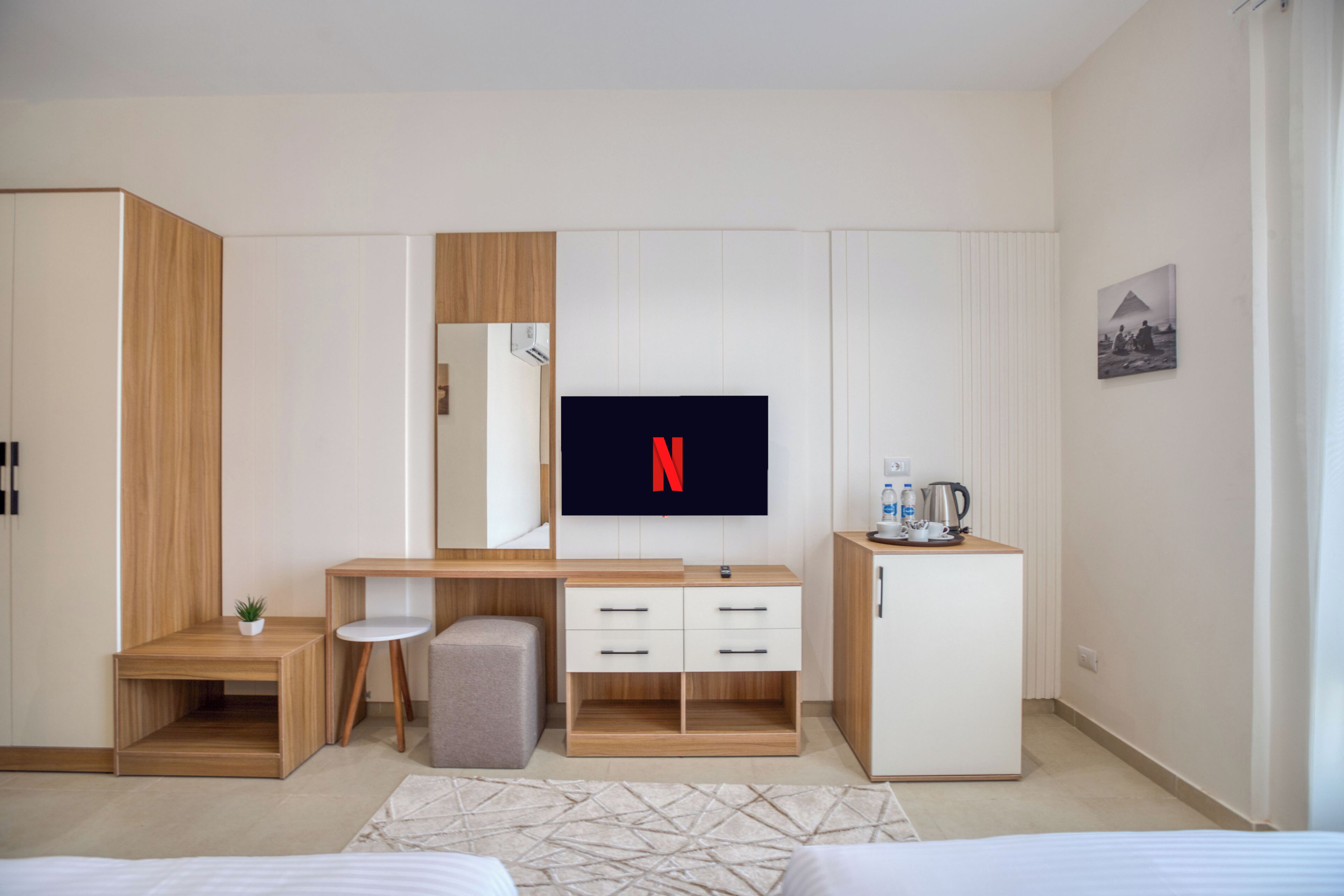 Habitación de hotel moderna con un escritorio de madera, un televisor mostrando el logotipo de Netflix, un taburete pequeño, un armario y una cama.