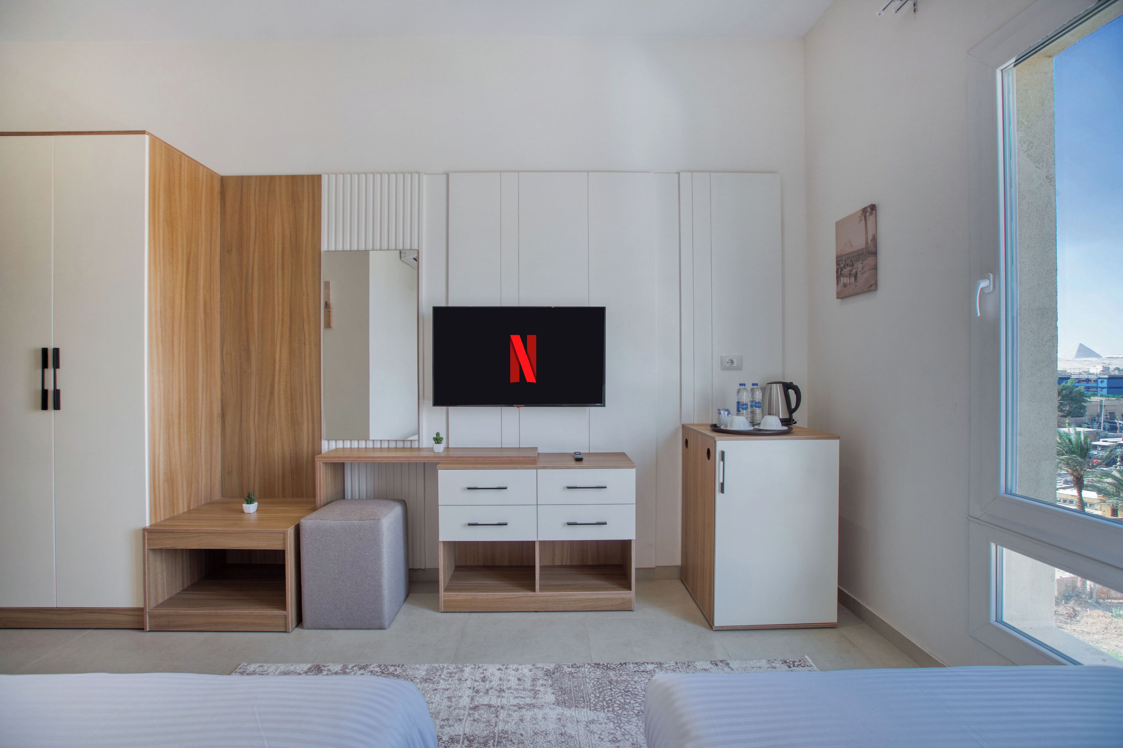 Una habitación de hotel moderna con un escritorio de madera, un televisor de pantalla plana, un minibar y un amplio ventanal con vistas a la ciudad.