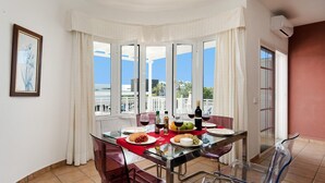 Un comedor con una mesa de vidrio, sillas de plástico transparente y un camino de mesa rojo. Hay platos con comida y botellas de vino.