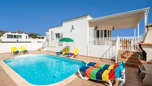 Una piscina con sillones de descanso y un área de patio techada.