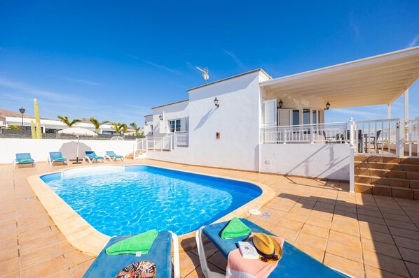 A swimming pool with lounge chairs and a covered area with steps leading to a white building. - Villa Gaida in Puerto Calero (Yaiza)