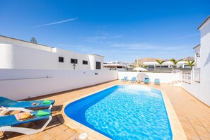 A swimming pool with lounge chairs and a white building in the background. - Villa Gaida in Puerto Calero (Yaiza)