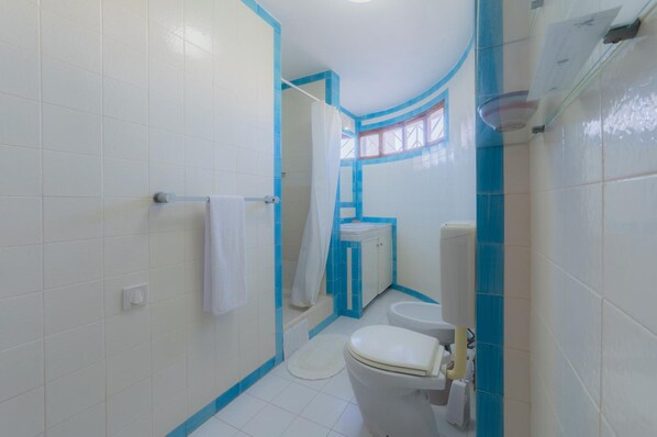 A bathroom with white tiles, a white toilet, a shower with a curtain, and a window. - Villa Mexico in Quarteira (Loulé)