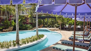 A pool area with lounge chairs and umbrellas, surrounded by tropical plants and a building in the background. - Classic Room with King Bed – Design-Centric Space (Honolulu)