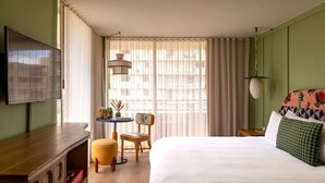 Ett hotellrum med en säng, ett skrivbord, en stol, en tv och ett fönster med gardiner.