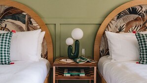 A hotel room with two beds, each with a checkered pillow, a small wooden nightstand between them, and a wall with a leaf pattern. - Pool House Studio with King Bed – Poolside Retreat (Honolulu)