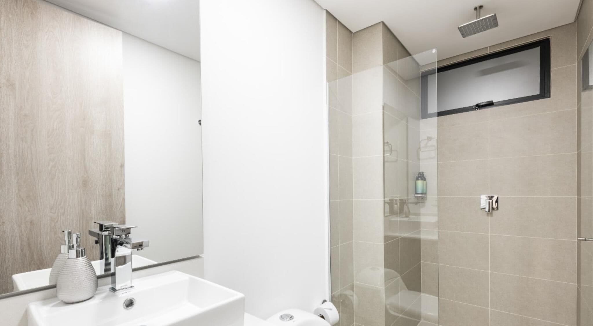 A modern bathroom with a white sink, mirror, and shower area.