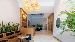 A modern reception area with a wooden reception desk, black seating, a small table with a book, and a large potted plant. - Kyux by Jalo (Medellín)