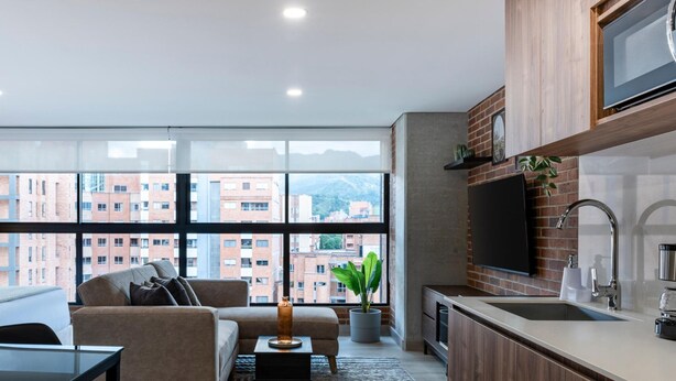 A modern apartment with a living area, kitchenette, and large windows offering city views. - Kyux by Jalo (Medellín)