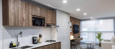 A modern kitchen with wooden cabinets, a built-in microwave, and a gas stove. There is a dining area with a table and chairs, and a sofa in the living room.